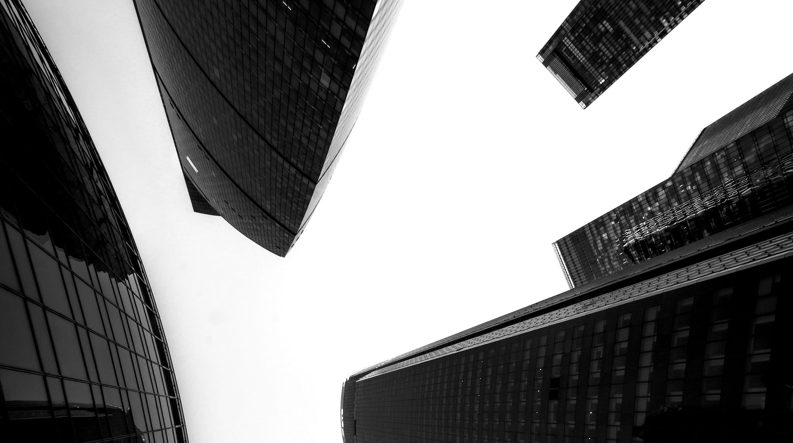 Dark glass towers seen from below against a white sky