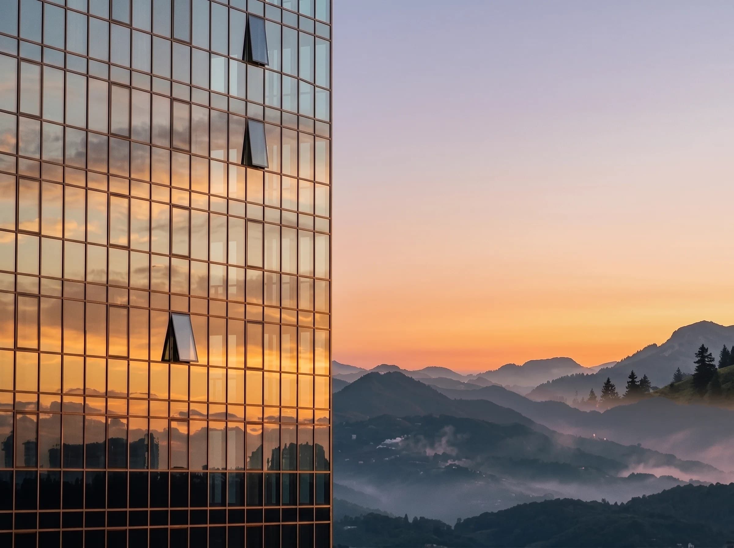 Glass façade reflecting a sunset over misty hills