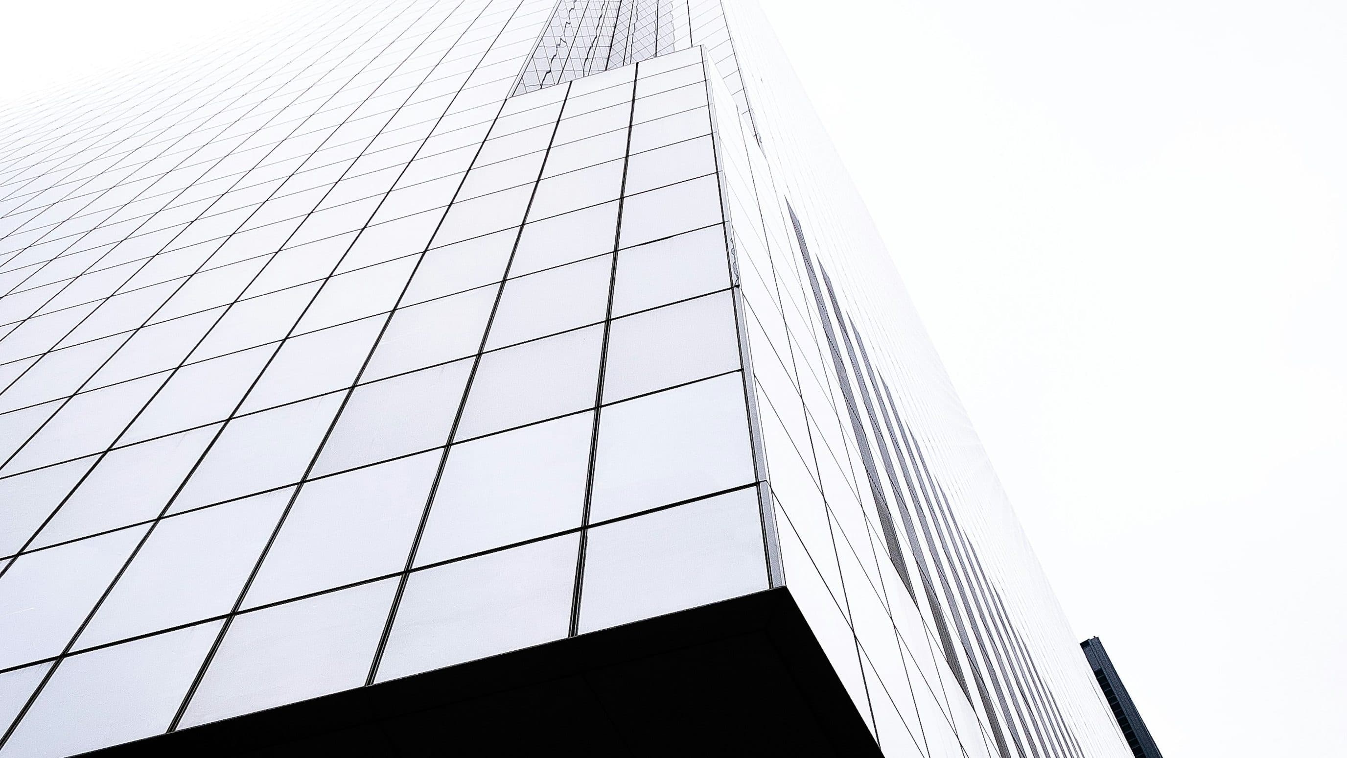 White glass tower seen from below against a pale sky